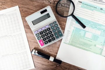 Papers, calculator, and marker sitting flat on a wooden desk